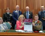 A photo of a group of people standing and sitting holding up a large piece of paper which says The Armed Forces Covenant on it.