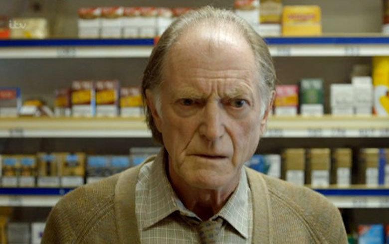 A close up image of a grey haired elderly man, actor David Bradley, in a shop looking shocked