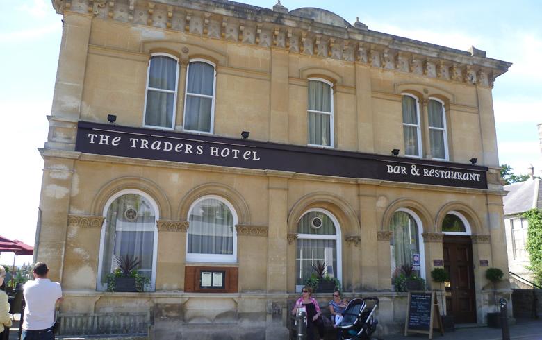 Exterior view of a grand stone building with a sign that reads Traders Hotel Bed and Breakfast above the windows