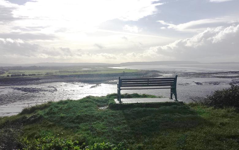 An empty bench sits overlooking a cliff and the sea coast at Clevedon