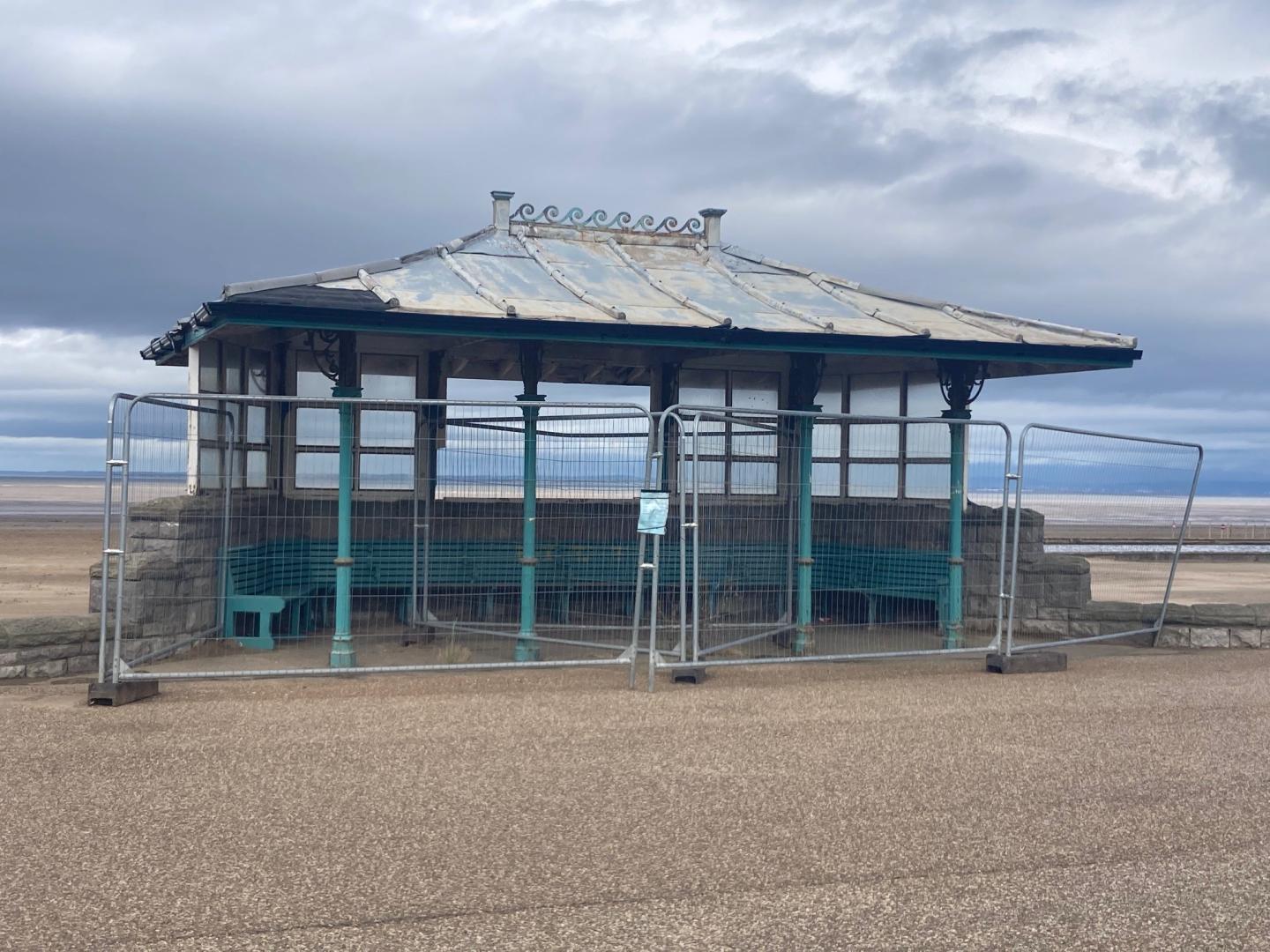 One of three Victorian seafront shelters in Weston-super-Mare surrounded by metal barriers with the beach in the background.