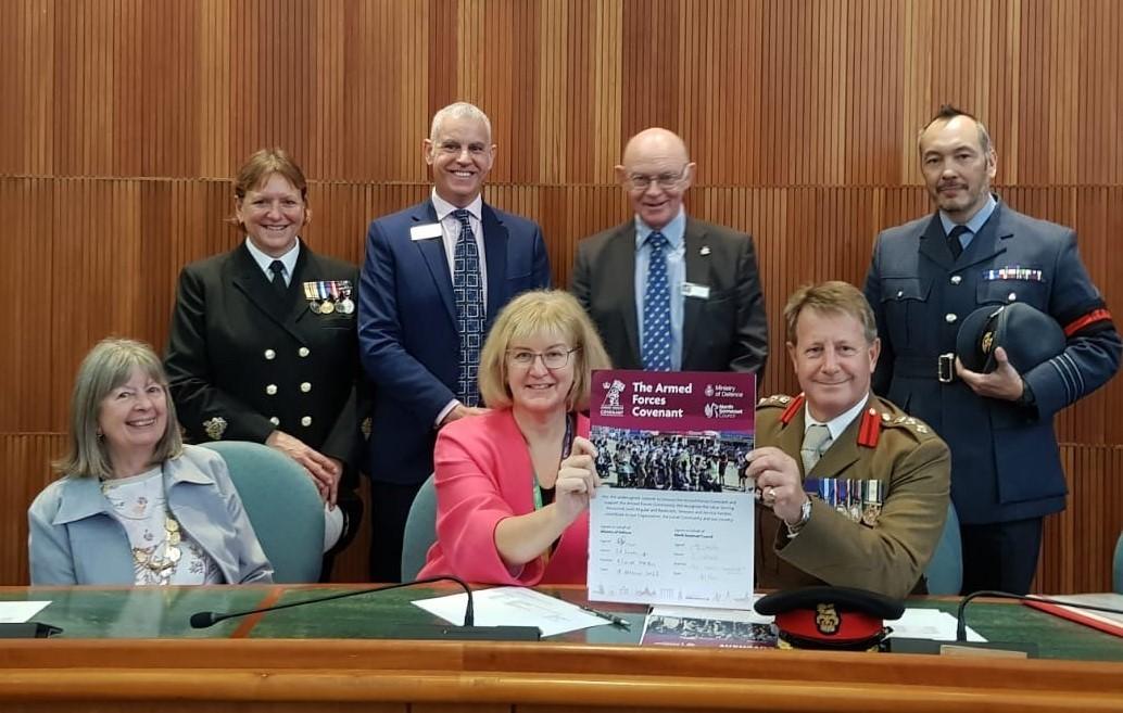 A photo of a group of people standing and sitting holding up a large piece of paper which says The Armed Forces Covenant on it.
