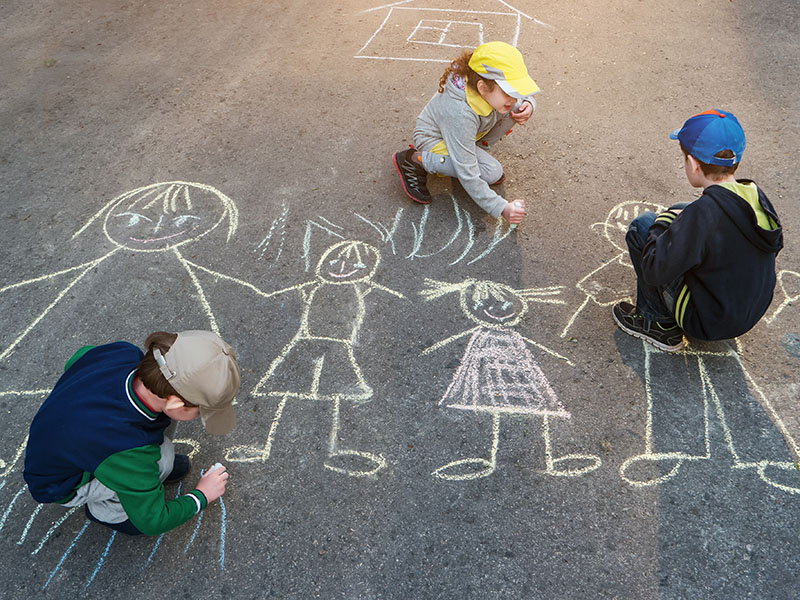 three children drawing a family with chalk on the road