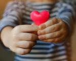 a child's hands holding a small pink heart towards the camera