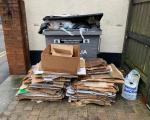 A photo of a large business waste container overflowing with rubbish and a large pile of cardboard in front