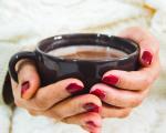 hands with red painted fingernails holding a warm drink in a black ceramic mug