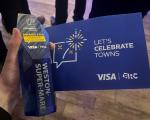 A blue glass award is held next to a blue card with 'Let's Celebrate Towns' printed on it