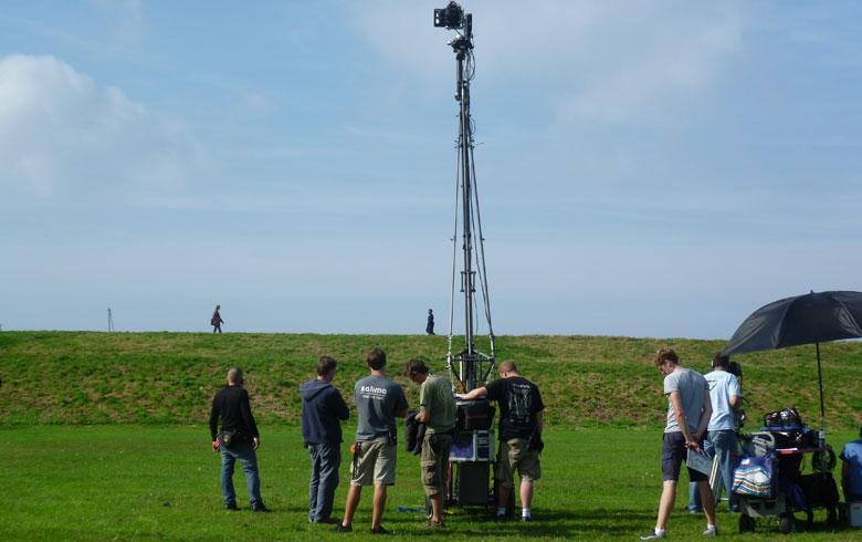 A tall camera crane being operated by camera crew in a large open green field