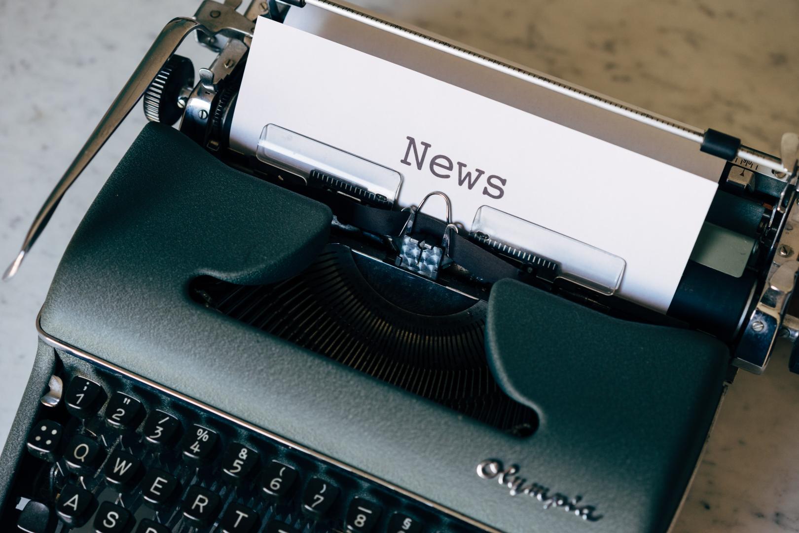 An old green typewriter with a piece of paper in it with the word News typed on it