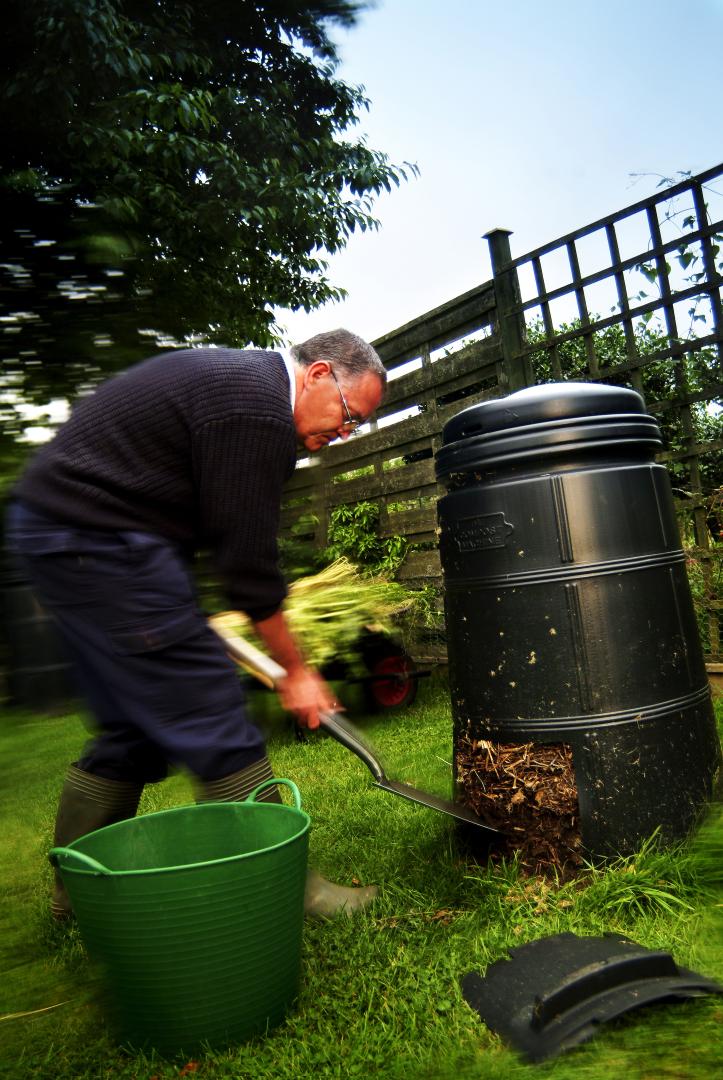 A photo of a man shovelling compost from the bottom of a compost bin
