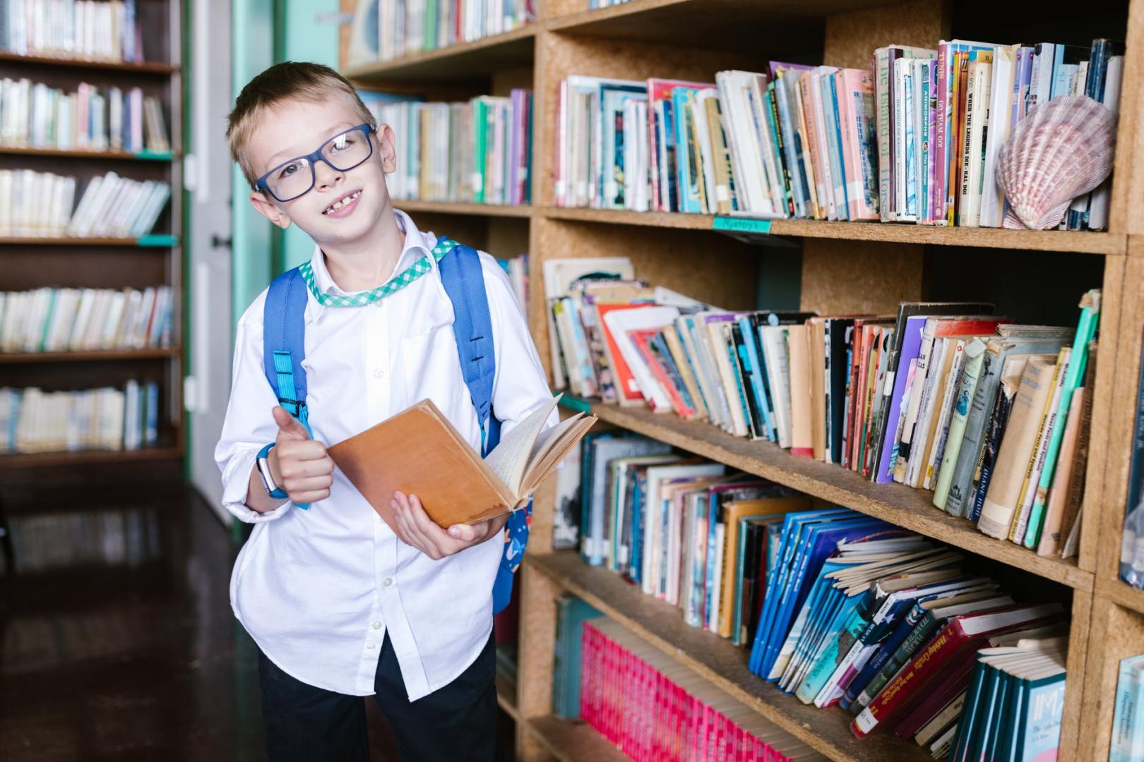 School girl in white long sleeve shirt holding brown book in library