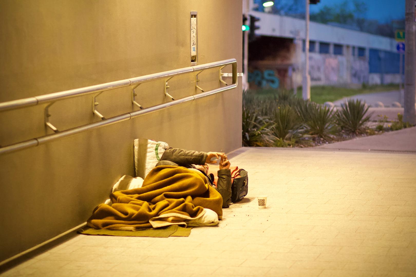 person sleeping rough under a blanket in a lit underpass