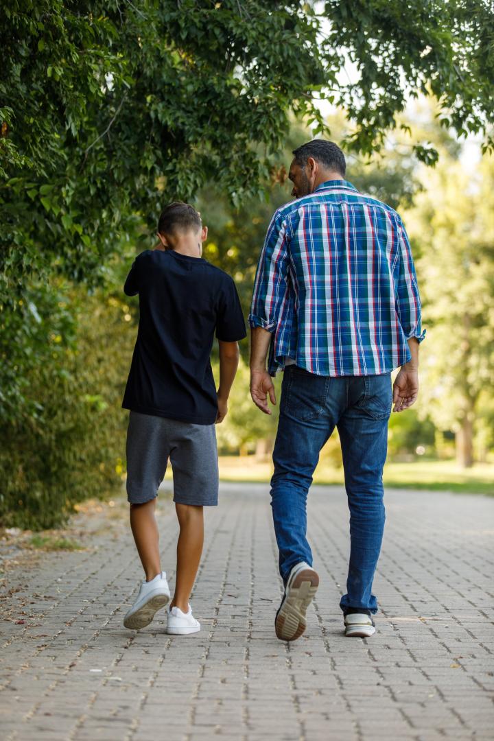 A photo of an adult man with boy walking in a park