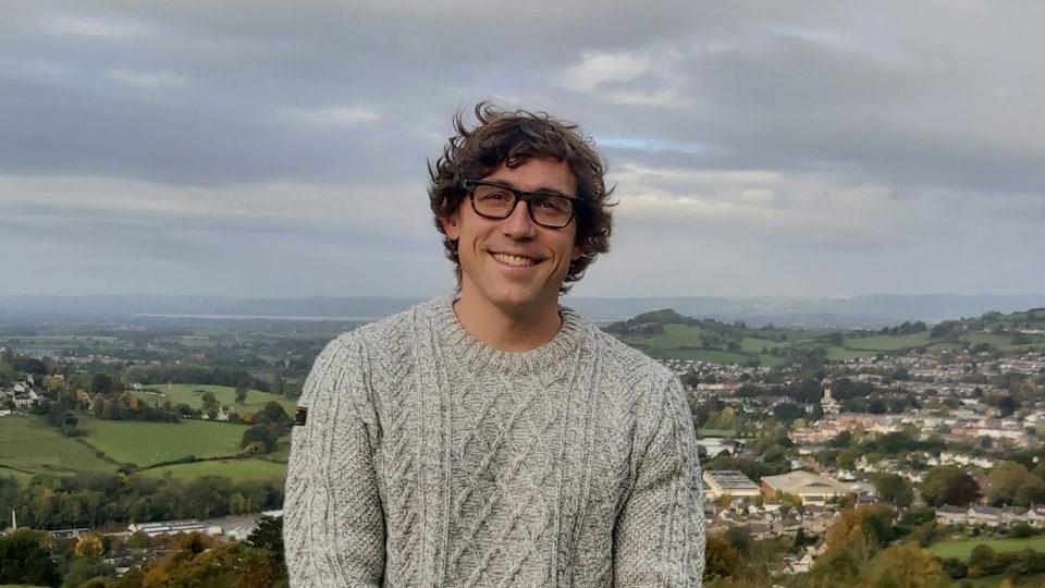 A photo of the children's author Tom Percival smiling with hills and countryside in the background