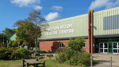 Hutton Moor Leisure Centre on a sunny day. A bench and trees are in front of the entrance